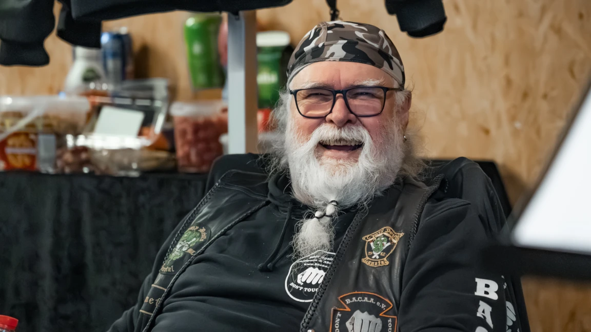 &Auml;lterer Mann mit Brille und Bandana bei der Motorradwelt 2026 Messe, l&auml;chelnd