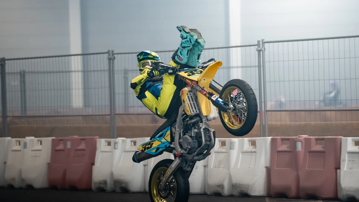 Motorradfahrer in Gelb und Blau macht einen Wheelie auf der Motorradwelt 2026 Messe
