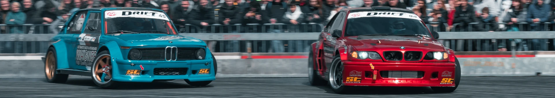 Zwei BMW Rennautos, turquoise und rot, w&auml;hrend einer Drift-Show auf der Tuning World Bodensee 2026.