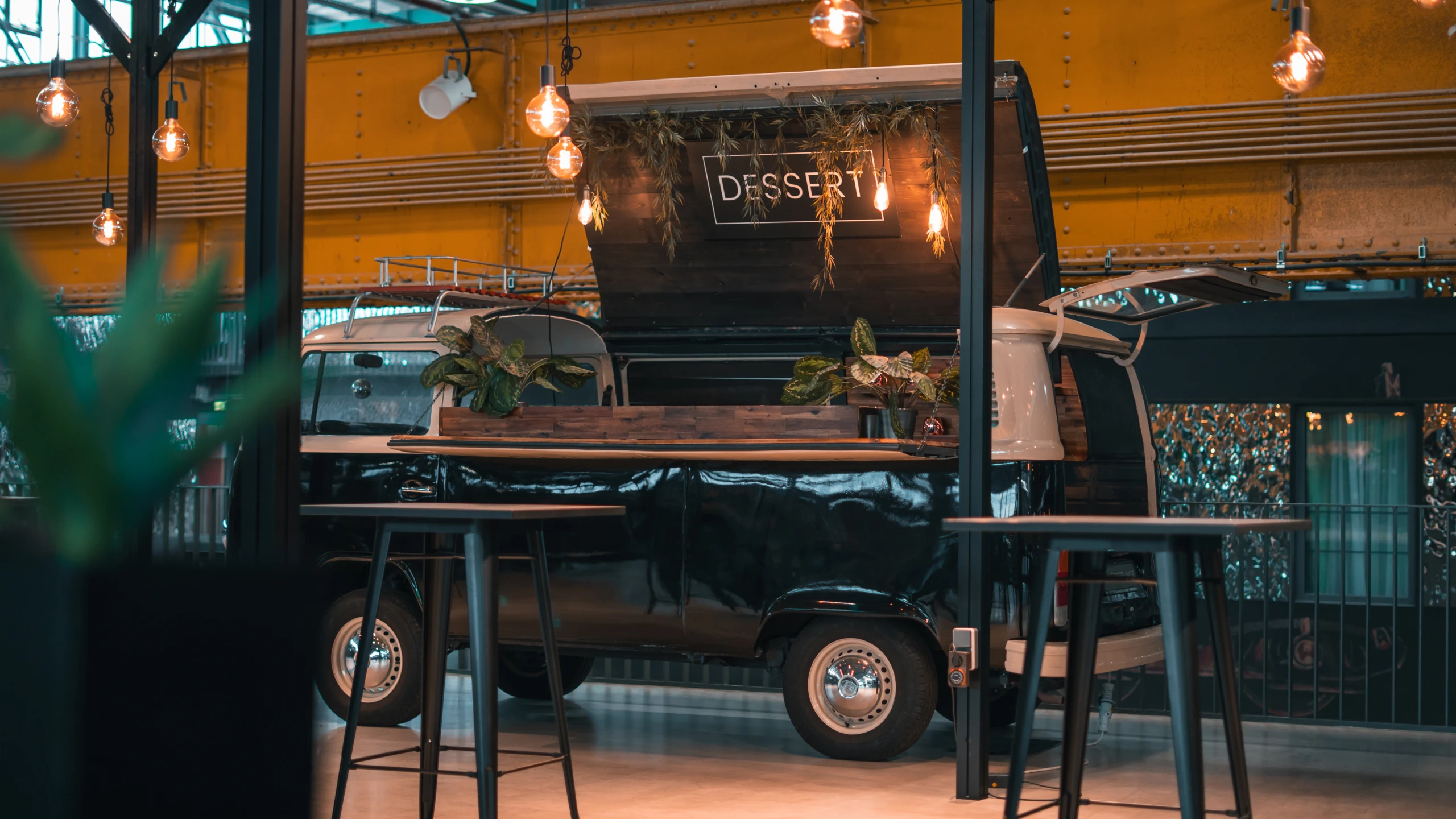 Food Truck mit Desserts im Innenbereich der Motorworld München Schwarzer Food Truck mit Pflanzen und Beleuchtung in der Motorworld München