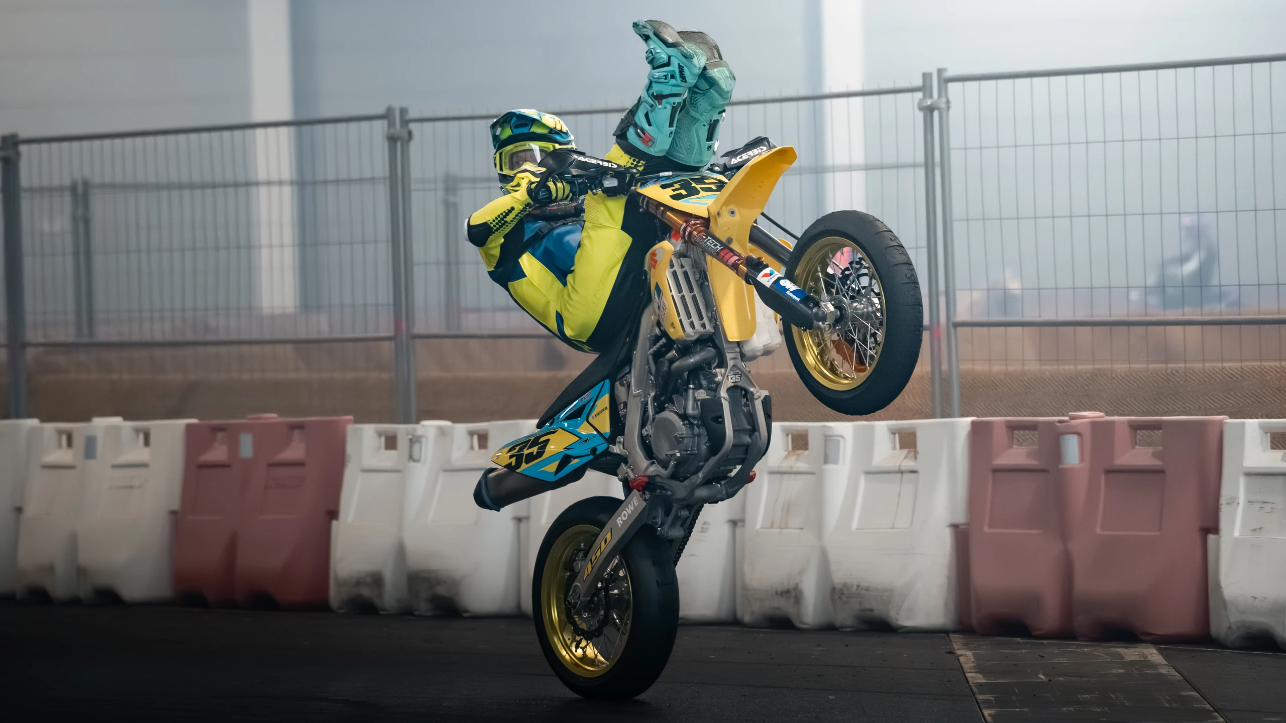 Motorradfahrer in Gelb und Blau macht einen Wheelie auf der Motorradwelt 2026 Messe