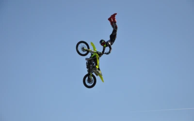 Motorradfahrer f&uuml;hrt einen Trickflug mit einem gelb-gr&uuml;nen Offroad-Motorrad aus.