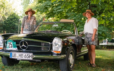 Zwei Frauen stehen neben einem schwarzen Mercedes-Benz 230SL auf der Lindau Klassik Rallye.