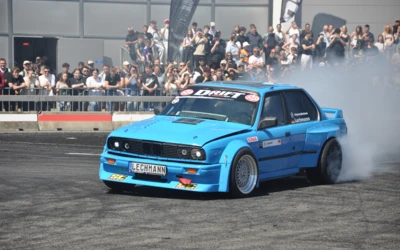 Blaue BMW E30 Limousine driftet auf der Tuning World 2025.