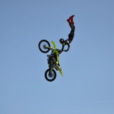 Motorradfahrer f&uuml;hrt einen Trickflug mit einem gelb-gr&uuml;nen Offroad-Motorrad aus.