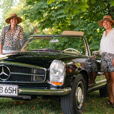 Zwei Frauen stehen neben einem schwarzen Mercedes-Benz 230SL auf der Lindau Klassik Rallye.