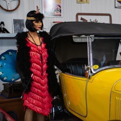 Mannequin in rotem Kleid steht neben gelbem Oldtimer im Automuseum