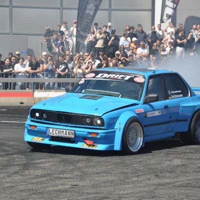Blaue BMW E30 Limousine driftet auf der Tuning World 2025.