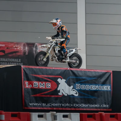 Fahrer in Schutzkleidung springt mit Motorrad &uuml;ber eine Rampe auf einer Messe.