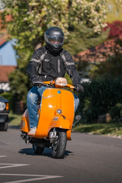 Mann f&auml;hrt auf orangefarbener Vespa, Umgebung bei Oldtimertreffen Wasserburg 2026
