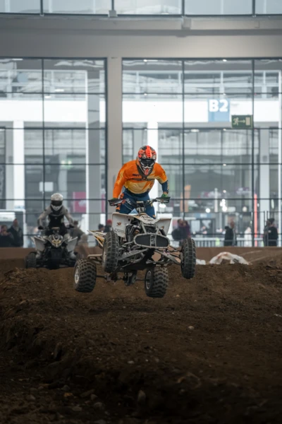 Motorradwelt 2026: Quadfahrer springt &uuml;ber einen Erdh&uuml;gel in einer Halle