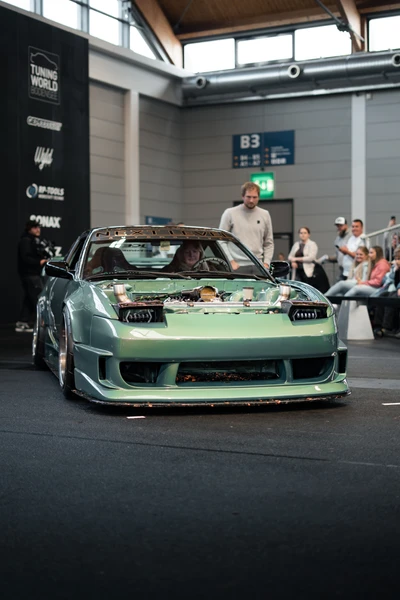 Person steht neben einem modifizierten gr&uuml;nen Auto auf der Tuning World Bodensee 2026