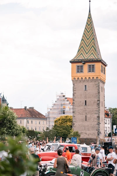 Menschen und klassische Fahrzeuge vor einem historischen Turm auf der Lindau-Klassik Rallye