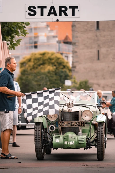 Start der Lindau-Klassik Rallye mit einem gr&uuml;nen Oldtimer und Startflagge