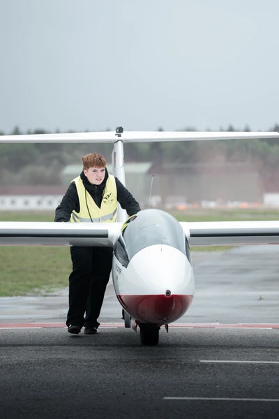 Person in Sicherheitsweste zieht ein Segelflugzeug auf dem Rollfeld