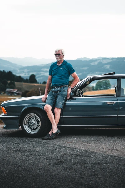 Person steht neben grauem Oldtimer auf Landstra&szlig;e bei Lindau-Klassik Rallye