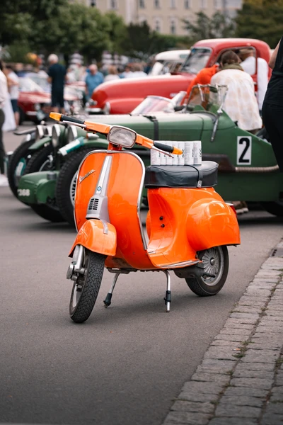 Orangefarbener Roller steht auf der Lindau-Klassik Rallye vor Oldtimern.