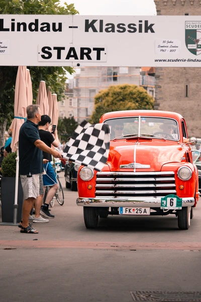 Roter Oldtimer f&auml;hrt unter dem Startbanner der Lindau-Klassik Rallye.