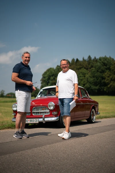 Zwei M&auml;nner stehen neben einem roten Auto auf einer Wiese w&auml;hrend der 10. Spa&szlig;rallye Bodensee 2026.