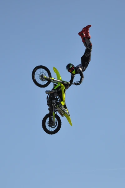 Motorradfahrer f&uuml;hrt einen Trickflug mit einem gelb-gr&uuml;nen Offroad-Motorrad aus.