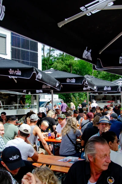 Menschenmenge auf dem American-Dream-V8 Treffen in Lindenberg, bewirtet unter Sonnenschirmen.