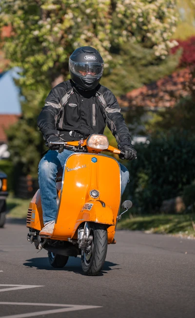 Mann f&auml;hrt auf orangefarbener Vespa, Umgebung bei Oldtimertreffen Wasserburg 2026