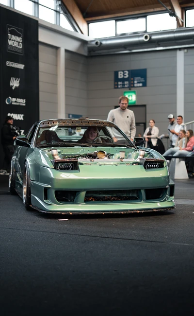 Person steht neben einem modifizierten gr&uuml;nen Auto auf der Tuning World Bodensee 2026