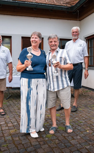 Paar h&auml;lt Pokale bei der Lindau-Klassik Rallye in einem Innenhof.