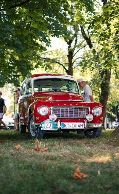 Roter Oldtimer auf der Lindau-Klassik Rallye, umgeben von B&auml;umen