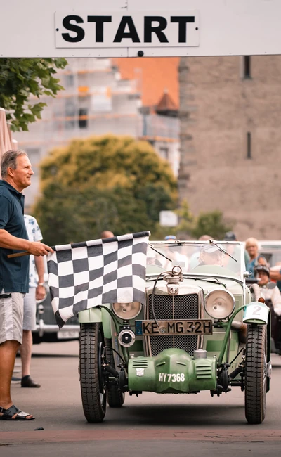 Start der Lindau-Klassik Rallye mit einem gr&uuml;nen Oldtimer und Startflagge