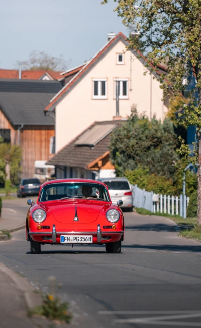 Roter Oldtimer f&auml;hrt entlang einer Wohnstra&szlig;e auf dem Oldtimertreffen Wasserburg 2026