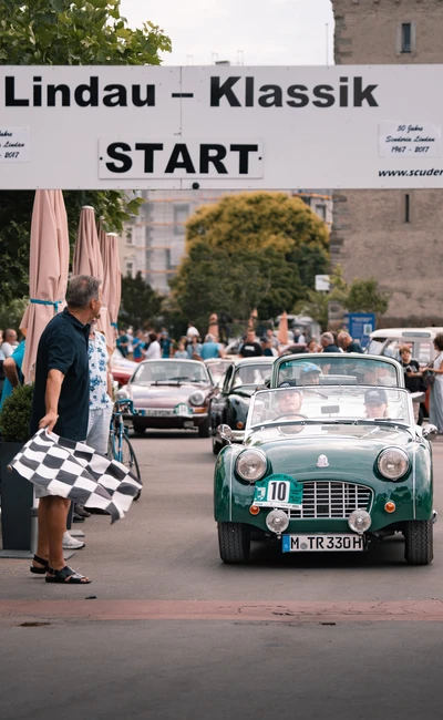 Gr&uuml;ner Sportwagen beim Start der Lindau-Klassik Rallye, Blockade mit Schachbrettflagge.