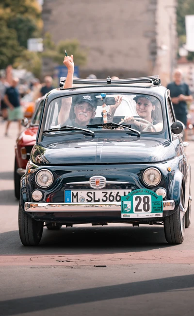 Blaue Fiat 500 f&auml;hrt mit drei Personen auf der Lindau-Klassik Rallye.