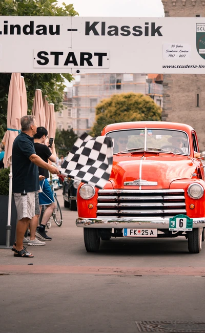 Roter Oldtimer f&auml;hrt unter dem Startbanner der Lindau-Klassik Rallye.