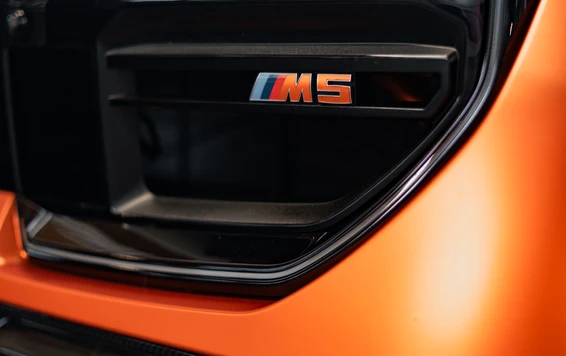 Nahaufnahme eines BMW M5 Emblems auf orangefarbenem Fahrzeug