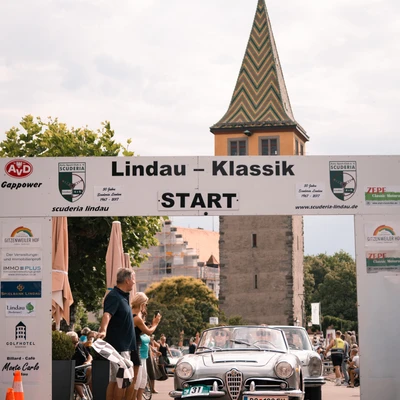 Oldtimer beim Start der Lindau-Klassik Rallye unter einem Torbogen.